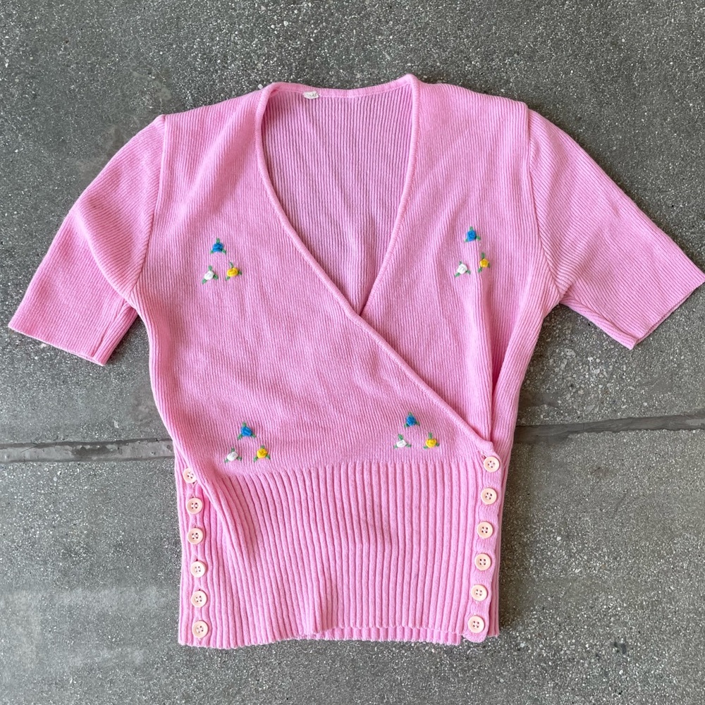 Vintage inspired pink v-neckline top with flower appliqué and button details.